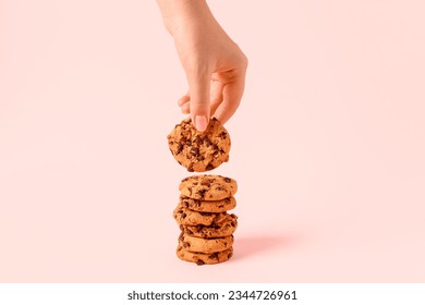 Woman taking tasty cookie with chocolate chips on pink background - Powered by Shutterstock