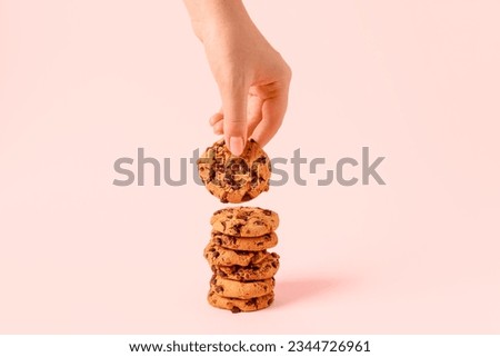 Woman taking tasty cookie with chocolate chips on pink background