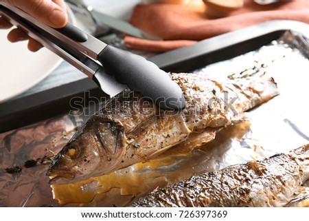 Woman taking tasty fish from baking tray using tongs, closeup
