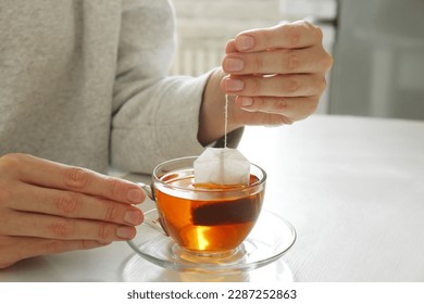 Woman taking tea bag out of cup at table indoors, closeup