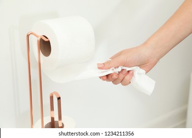 Woman taking toilet paper from roll holder in bathroom, closeup