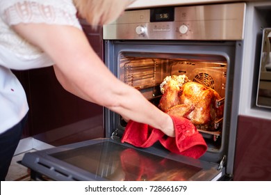 Woman Taking Turkey Out Of Oven On A Kitchen Background. Roasted, Traditional Turkey Cooking. Christmas Turkey.