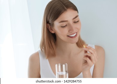 Woman Taking Vitamin Pill With Glass Of Fresh Water Indoors. Smiling Girl Taking Omega 3 Fish Oil Capsule, Vitamin Supplement. Diet Nutrition Concept