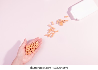 Woman Taking Vitamins And Supplements. Orange Vitamin Capsules Or Pills In Woman Hand Pouring From White Bottle. Healthy Lifestyle, Top View, Pastel Background