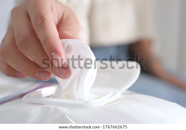 Woman taking wet wipe out of pack against blurred
background, closeup