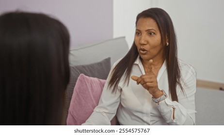 Woman talking to daughter in living room suggesting family conversation at home with adult and child seated on couch - Powered by Shutterstock