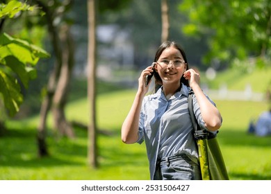 A woman is talking on her cell phone while walking in a park. She is wearing glasses and a striped shirt - Powered by Shutterstock