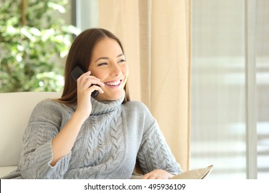 Woman Talking On A Land Line Phone Sitting On A Sofa In The Living Room At Home