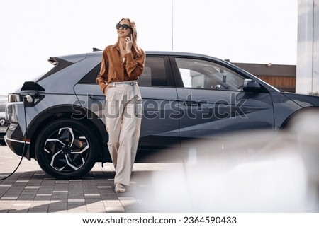 Woman talking on the phone by her electric car