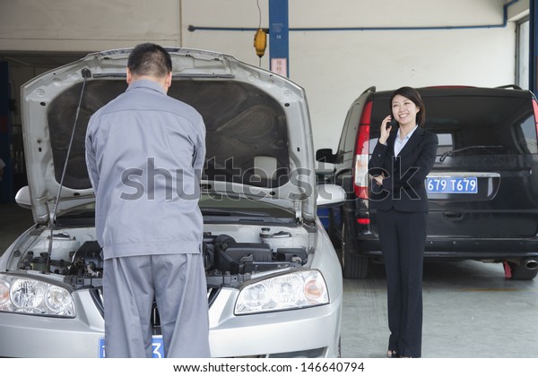 Woman\
Talking on Phone While Mechanic Fixes Her\
Car