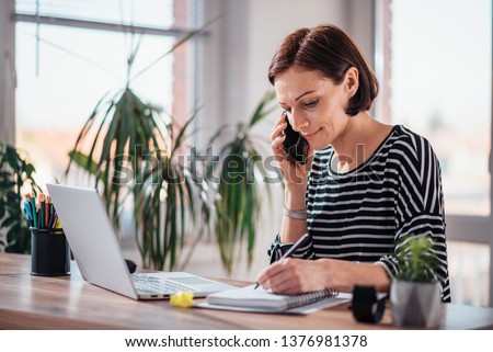 Woman talking on the smart phone and writing notes in notebook in the office