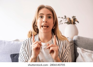 Woman talking and pointing while explaining on couch at home, casual blonde vlogger expressing excitement and emphasis
