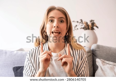 Woman talking and pointing while explaining on couch at home, casual blonde vlogger expressing excitement and emphasis
