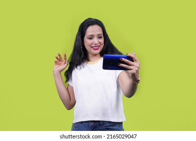 Woman Talking In Video Call Waving Hands. Excited Joyful Beautiful Indian Girl Or Young South Asian Woman Wearing White T Shirt Standing Doing Selfie Shot On Mobile Phone.