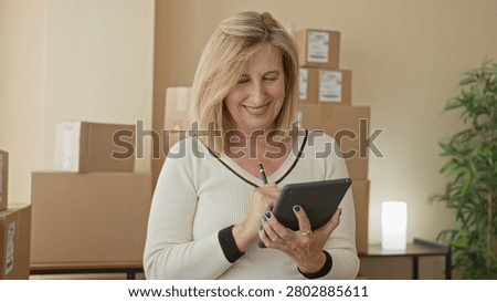 Woman tapping tablet with hands while checking packages and parcels in a smallbusiness building; entrepreneurial planning contentment.