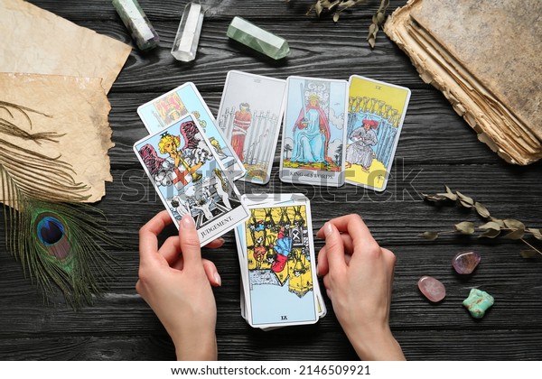 Woman\
with tarot cards at black wooden table, top\
view