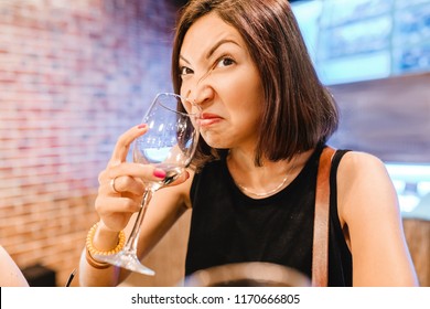 A Woman At The Tasting Tries And Smells The Aroma Of An Ugly Glass Of Wine. Concept Of Alcoholism And Spoiled Drink