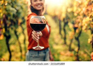 Woman tasting wine in vineyard. She is showing glass of wine to camera.