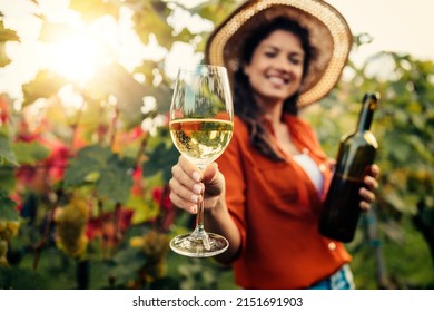 Woman tasting wine in vineyard. She is showing glass of wine to camera. - Powered by Shutterstock