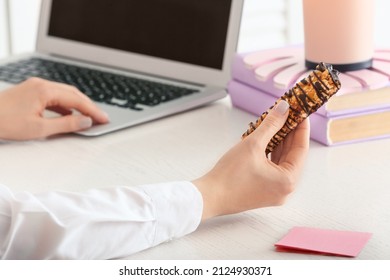 Woman With Tasty Chocolate Nut Bar Sitting At Workplace In Office