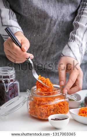 Woman with tasty fermented carrot in glass jar at table, closeup