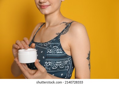 Woman With Tattoo Holding Jar Of Cream Against Yellow Background, Closeup
