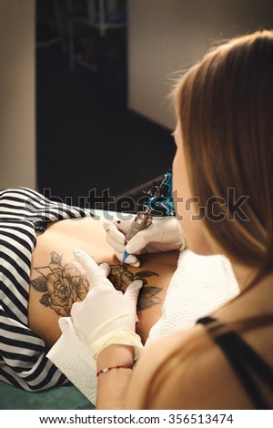 Woman tattooer make tattoo with black roses on a woman stomach.