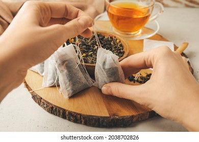 Woman with tea bags and dry leaves on light background