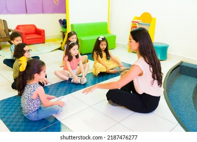 Woman teacher explaining a school activity and meditation exercises and yoga to her preschool students sitting on the kindergarten floor - Powered by Shutterstock