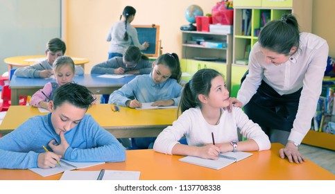 Woman Teacher Helping Drawing To Group Kids 9-10 Years Old At Class. Focus On Boy