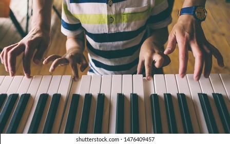 A Woman Teaches Her Son To Play The Piano. The Boy Masters The Keyboard Musical Instrument. A Child Learns Music. Children's And Women's Hands On The Piano Keys. Music Lesson. Tutor For A Child.