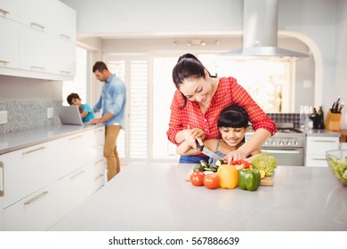 Woman teaching daughter to cut vegetables at table in house - Powered by Shutterstock