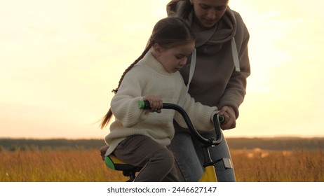 Woman teaching girl to ride bike, silhouettes at sunrise in field. Emotional support, participation, presence and encouragement from mother in learning process to help child overcome fear of failure. - Powered by Shutterstock