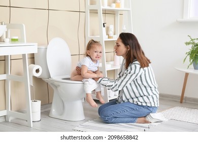 Woman teaching her baby to use toilet bowl in bathroom