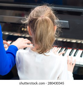 Woman Teaching Little Girl To Play The Piano. Back View.