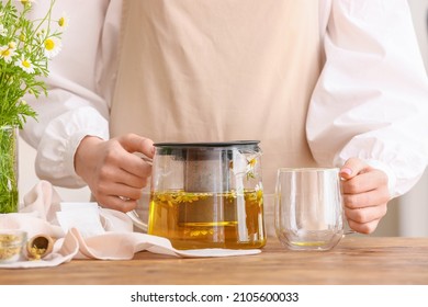 Woman With Teapot Of Fresh Chamomile Tea And Cup On Wooden Table