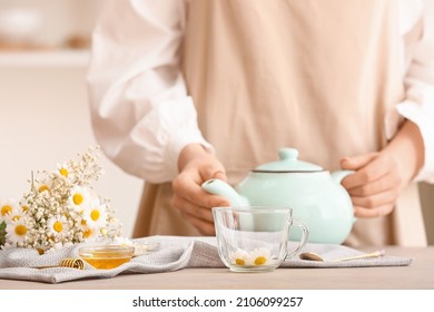 Woman With Teapot Of Tasty Chamomile Tea On Table