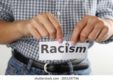 Woman Tearing Up Paper Sheet With Word Racism On White Background, Closeup