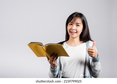 Woman teen smiling holding open book and show thumb up finger for good sign, Portrait of beautiful Asian young female person learn success studio shot isolated on white background, education concept