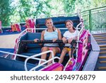 A woman and a teenage girl smiling while riding a fun amusement park ride at a theme park or carnival. Laughing and having fun together during a summer vacation