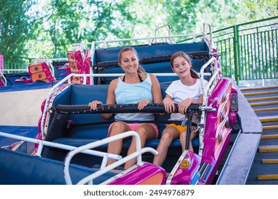 A woman and a teenage girl smiling while riding a fun amusement park ride at a theme park or carnival. Laughing and having fun together during a summer vacation - Powered by Shutterstock