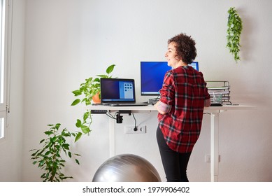 Woman Telecommuting At An Adjustable Desk Standing Next To A Fitball