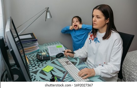 Woman Telecommuting Making A Video Conference With Her Daughter Grimacing Behind. Selective Focus On Woman In Foreground