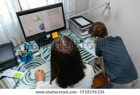 Woman teleworking at home while her son studies next to her
