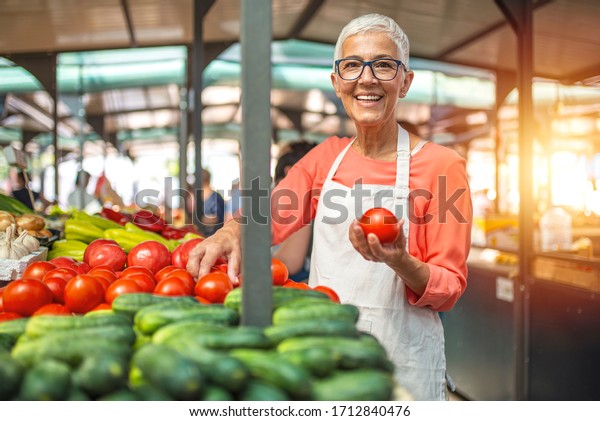 Woman tending an organic vegetable stall at a\
farmer\'s market and selling fresh vegetables. Female gardener\
selling organic crops and picking up a bountiful basket full of\
fresh produce. Only\
organic.