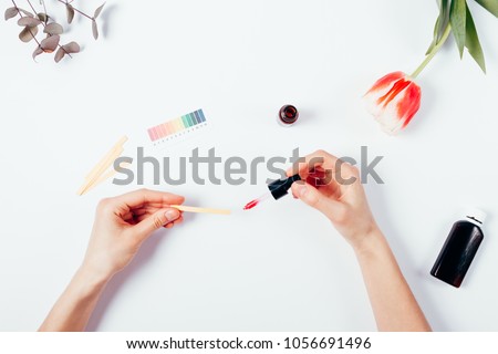 Woman testing cosmetics by using litmus paper. Top view of female hands on white background, applying with a pipette serum into a litmus test paper. Determination of pH level in cosmetics