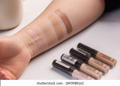 Woman testing different shades of liquid foundation on her hand and tubes with concealer closeup.