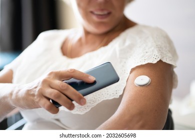 Woman Testing Glucose Level With Continuous Glucose Monitor On Mobile Phone