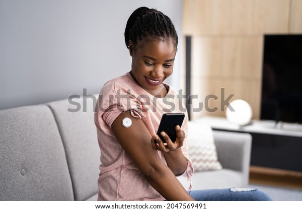Woman Testing Glucose Level With Continuous Glucose\
Monitor On Mobile Phone