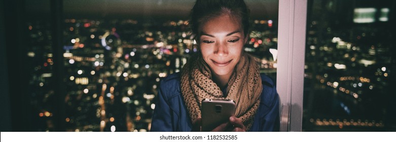 Woman Texting Instant Messaging Text On Mobile Phone Online At Night - Bright Light From Screen Illuminating Young Asian Girl In London City Background Banner Panorama.